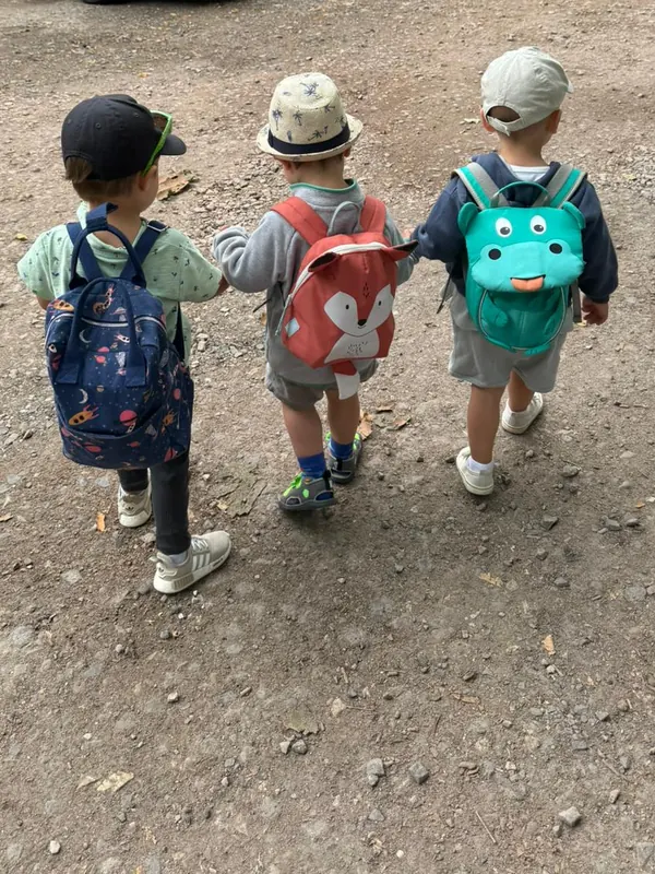 Drei Tageskinder mit Kindergartenrucksäcken Hand in Hand